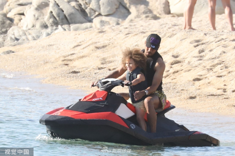 奥巴梅扬与儿子在浅滩边嬉戏玩水，足球置于身旁，展现了训练之余温馨愉快的家庭互动瞬间