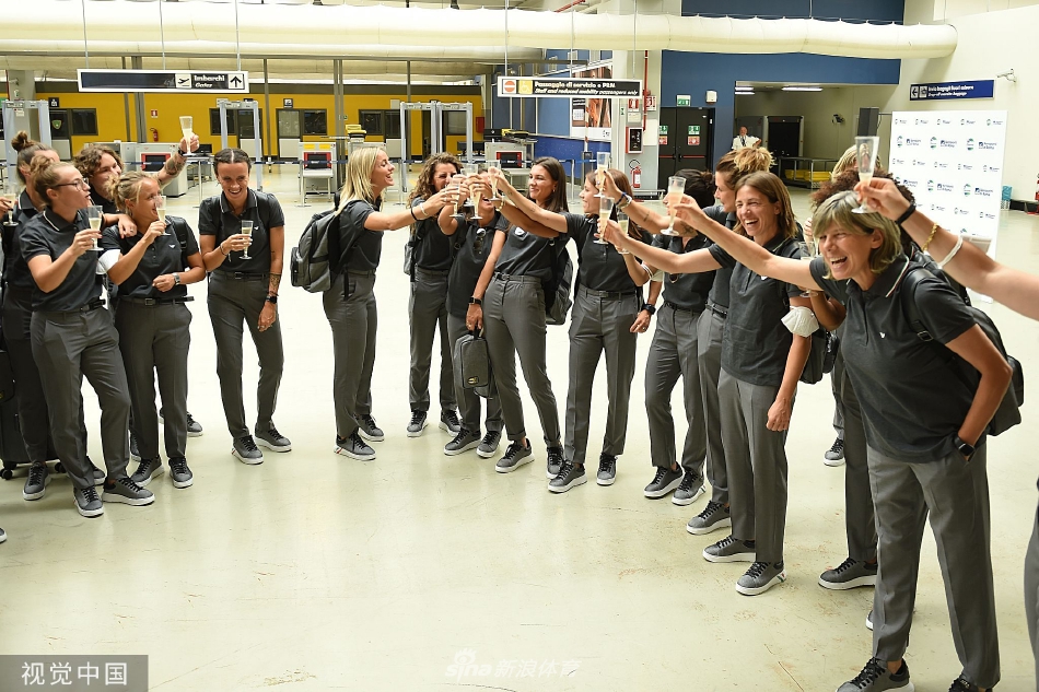 两位女足姑娘在机场登机口前并肩而立，望向相同的远方，背影挺拔而充满力量，象征着她们将共同面对前方的挑战。