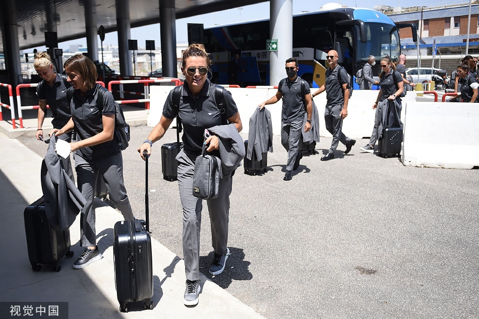 全队成员在机场合影留念，统一的深色西装下是鲜艳的领带或丝巾，每个人脸上都洋溢着自信的笑容，定格下出征时刻的团结与朝气。