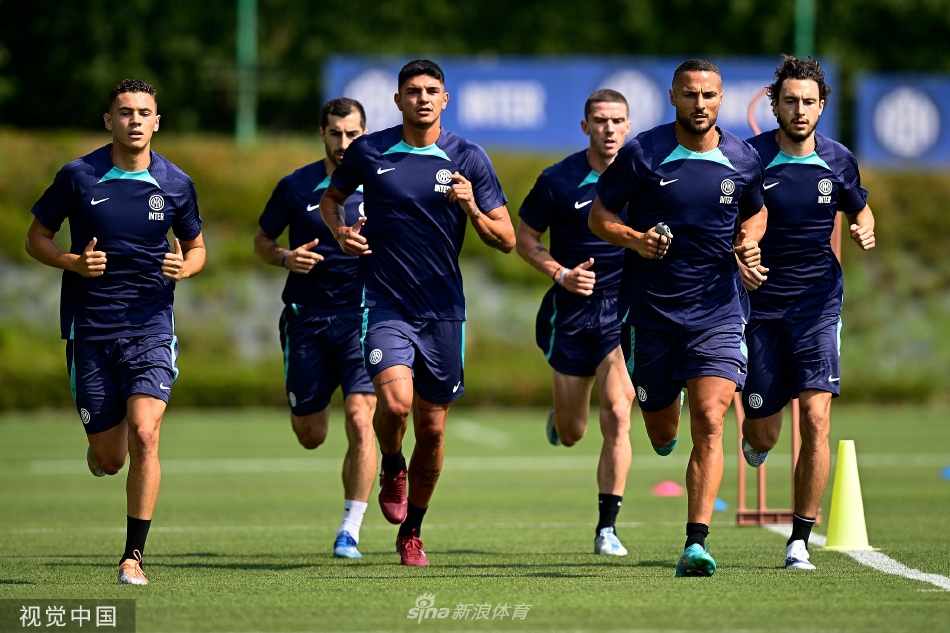 球员们沿着训练场边线匀速前进，身后是郁郁葱葱的树木，构成一幅充满活力与希望的夏日训练图景。