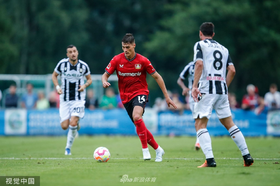 教练席特写，勒沃库森主帅手持战术板神情专注地注视赛场，助理教练在一旁激动地比划讲解