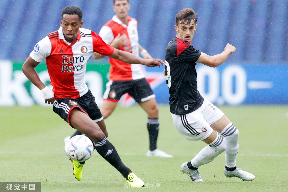 奥萨苏纳球员绝杀后张开双臂奔向角旗区庆祝，背影映衬着夕阳与失望的主场球迷。