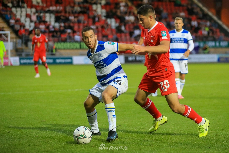 女王公园巡游者球迷看台上，一位小球迷趴在栏杆上望向球场，眼神中充满对主队下一次进攻的期待，周围的大人们或鼓掌或呐喊，足球的激情在此传承。