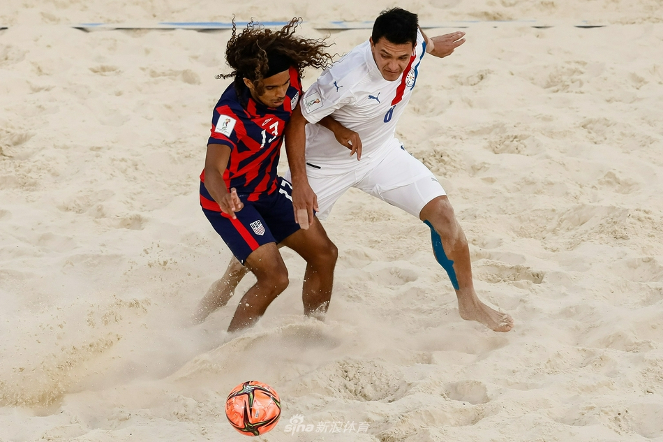 一名巴拉圭球员在队友的帮助下高高跃起，准备来一记势大力沉的倒挂金钩，他的身影在莫斯科的阳光下投射在柔软的沙地上。