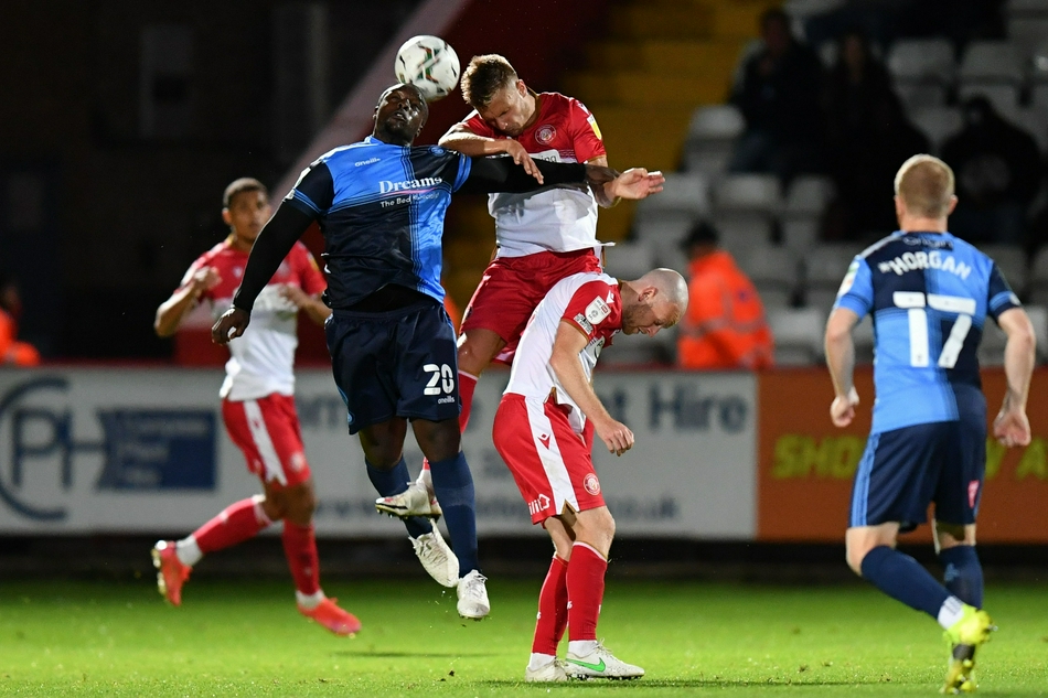 韦康比流浪者的球员们在德巴尔罚入制胜点球后围成一圈，振臂高呼，激情庆祝这场来之不易的胜利，而斯蒂夫尼奇的球员们则黯然神伤，形成鲜明对比。