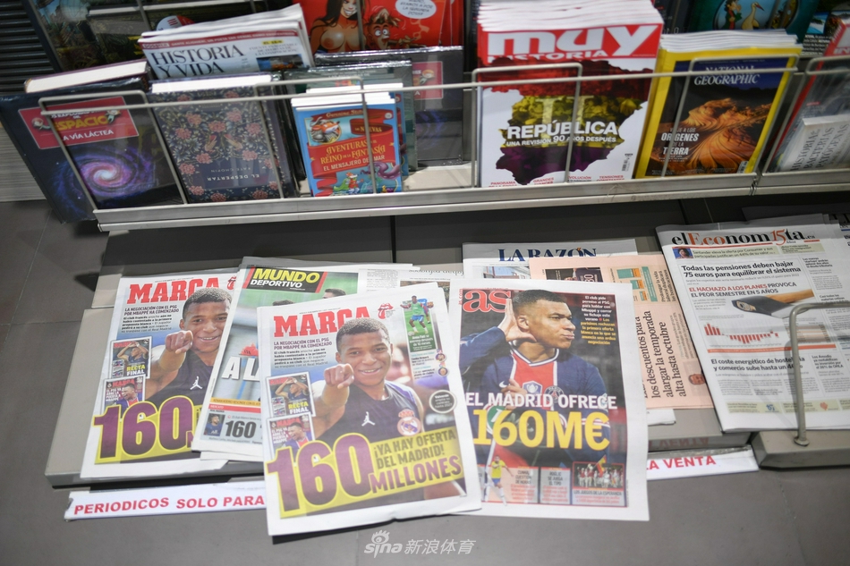 在西班牙报纸的头版上，姆巴佩身着法国队深色训练服，神情专注而坚定。巨大的黑色标题虽被遮挡，却更激起读者的好奇，仿佛他正透过新闻纸的油墨，凝视着自己梦寐以求的伯纳乌球场。