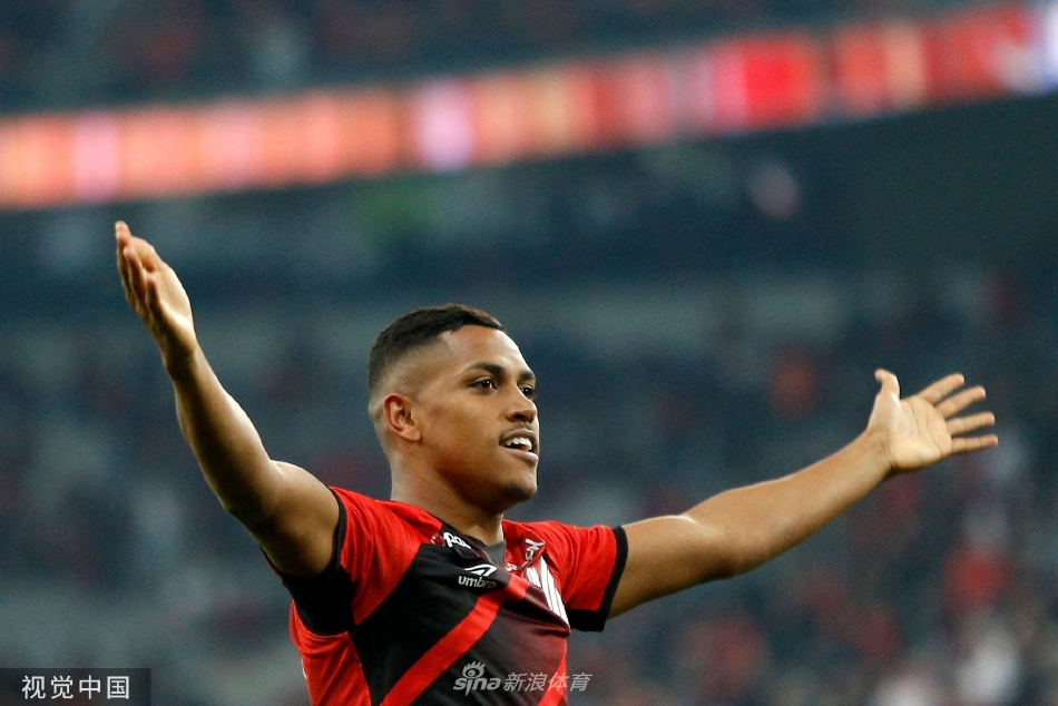 巴拉纳竞技前锋如猎豹般带球疾驰，面对两名防守球员的夹击，他身体倾斜，球衣飘扬，展现了南美足球特有的灵动与突破勇气。