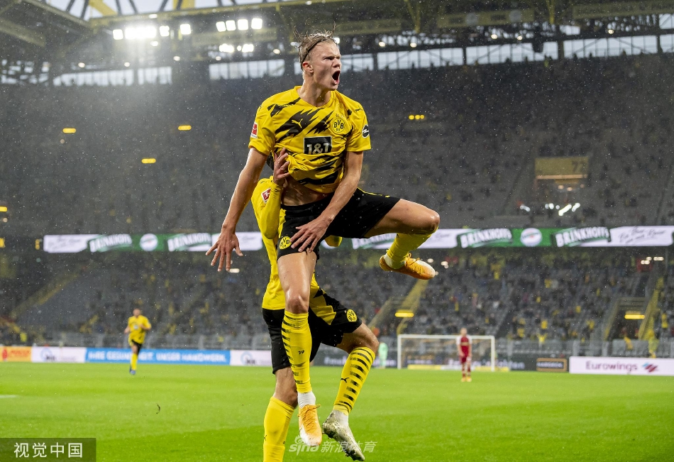 哈兰德与曼城俱乐部代表在签约桌前握手，背景是曼城天蓝色旗帜，定格了这历史性合作瞬间