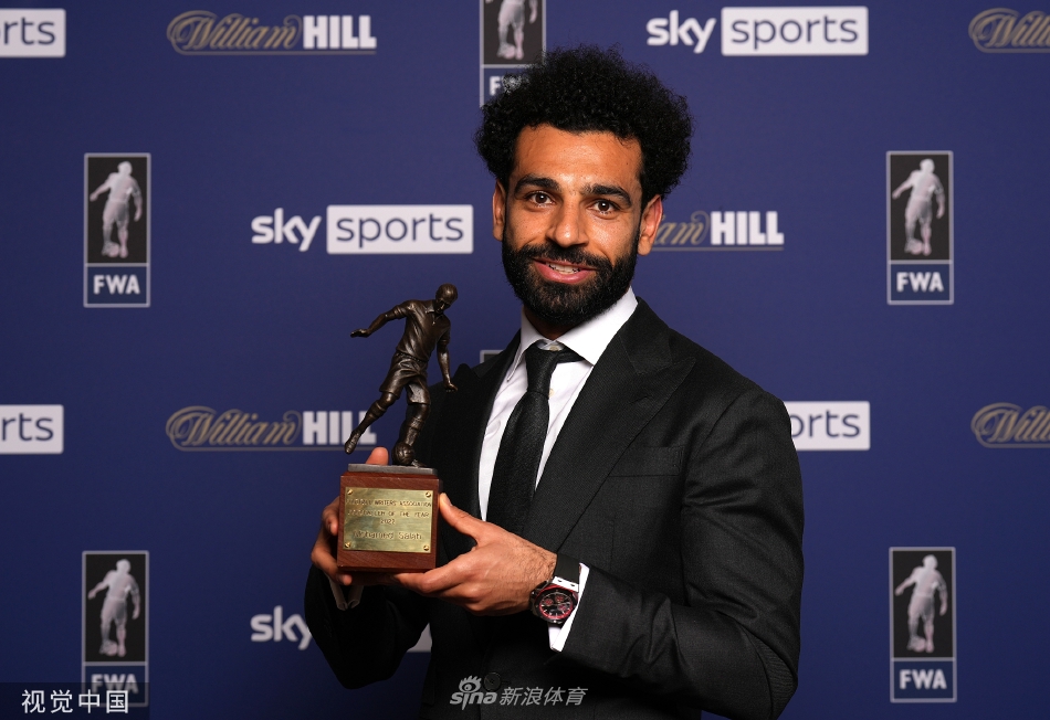 萨拉赫在颁奖典礼上手捧年度最佳球员奖杯，脸上洋溢着自豪与喜悦的笑容，奖杯的灯光映亮了他专注的目光。