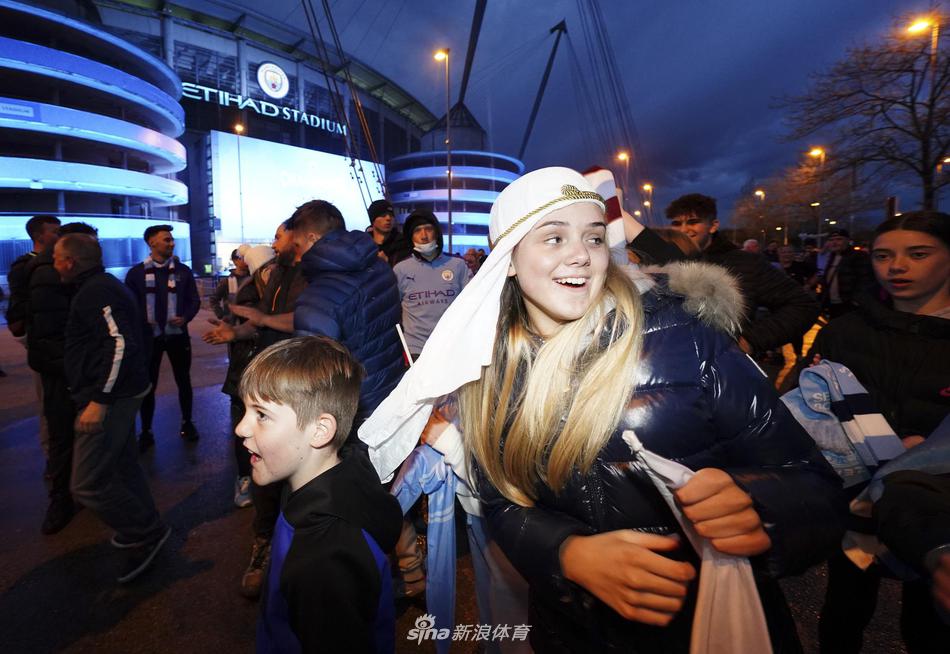 人山人海的慶祝隊伍中，一位父親將年幼的孩子高高舉過頭頂，讓他騎在自己的肩頭。孩子手中揮舞著一條小小的曼城圍巾，這一幕溫情與激情交織，象徵著俱樂部榮耀的代代相傳。