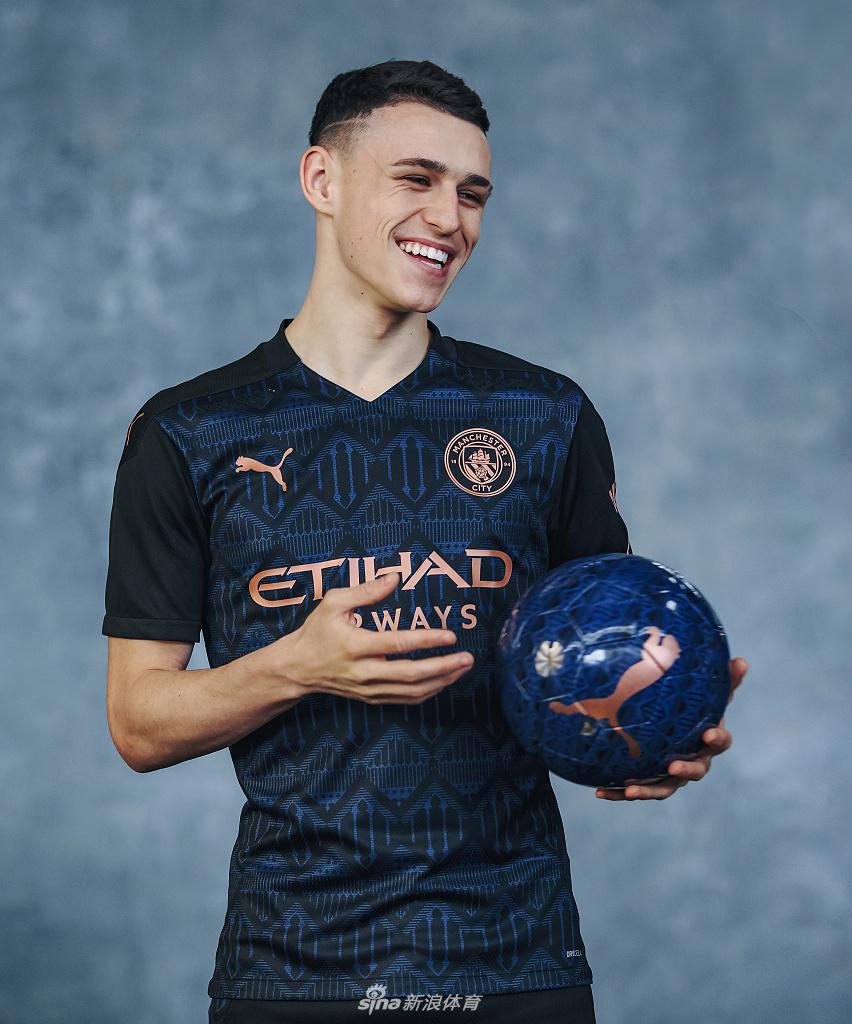 贝尔纳多·席尔瓦在镜头前露出标志性的温暖笑容，新球衣上的铜色队徽在他胸前闪耀，仿佛一枚勋章。背景虚化的光线化作点点光斑，如同胜利的纸屑在空中飘洒，定格了他在新赛季蓄势待发的喜悦瞬间。