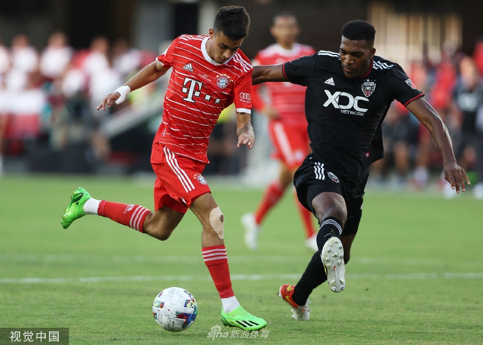 夜幕下的足球场灯光如昼，双方球员在中场展开激烈争夺，皮球在空中划出一道清晰的轨迹。