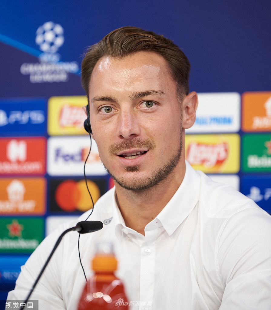 发布会上，主帅紧握双拳，身体微微前倾，对着话筒阐述着球队的战术哲学。他深邃的目光仿佛已穿透镜头，洞悉了明晚比赛场上可能发生的一切。身后的球队徽章在灯光下熠熠生辉，见证着这支青年军成长的每一个坚实脚印。