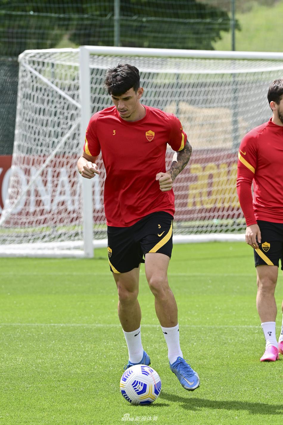 主教练在场边双手插兜，神情严峻地注视着场上的训练情况，他的身后是教练组和替补球员，远处的训练塔楼清晰可见。