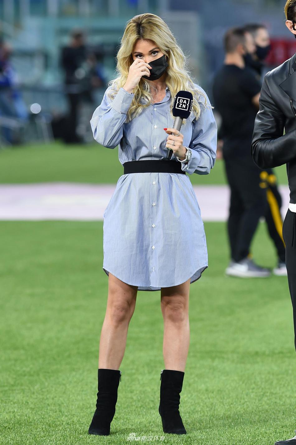 莱奥塔在场边进行报道工作，她神情专注地对着镜头，即便在人声鼎沸的球场中，也展现出极佳的专业素养。