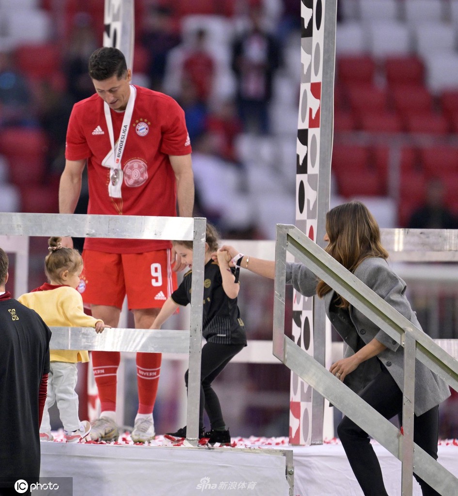 莱万蹲在绿茵场上，深情拥抱穿着白色连衣裙的小女儿，眼神里充满无尽宠溺