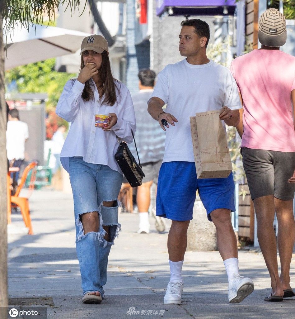 二人站在街边小食店前，似乎在认真挑选食物，超模女友微微前倾身体，展现出优美的侧影线条，埃尔南德斯则在一旁耐心陪伴