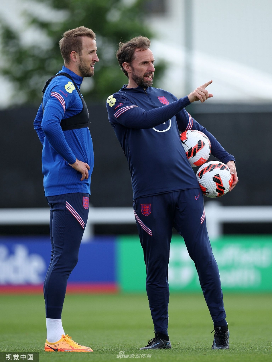训练场上，英格兰队长哈里·凯恩正与主教练索斯盖特并肩而立，进行着深入的交谈。凯恩神情专注，手指向球场方向，似乎在分析战术细节，而索斯盖特则环抱双臂，侧耳倾听，两人的交流充满了信任与默契。