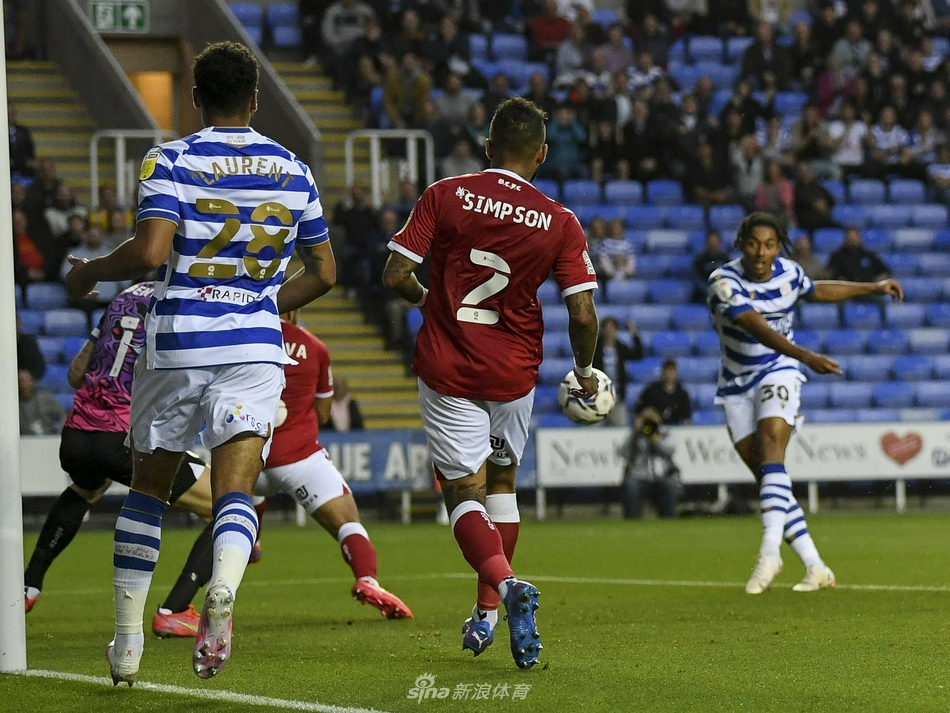 雷丁与布里斯托尔城的球员们在中圈弧附近激烈拼抢，客队球员的白衣在夜色下格外醒目，瞬间的肌肉对抗定格了比赛的紧张与胶着