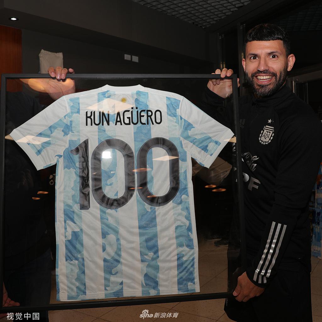 梅西与阿圭罗并肩而立，手中各自拿着自己的纪念球衣，两人相视而笑，眼神中充满了对彼此的祝福与多年战友的默契。