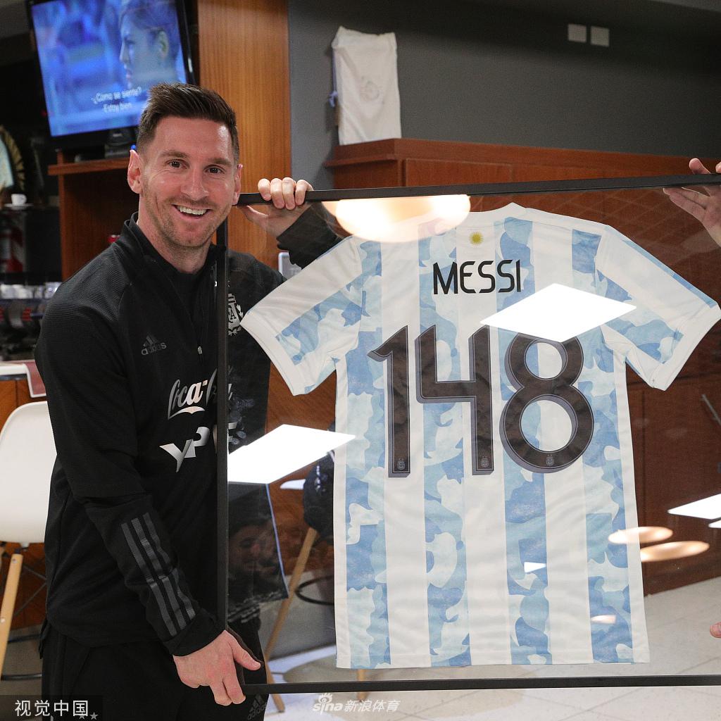梅西手捧纪念球衣，微笑中带着一丝腼腆，这件印有“148”号码的战袍象征着他成为阿根廷队史出场第一人的辉煌成就。