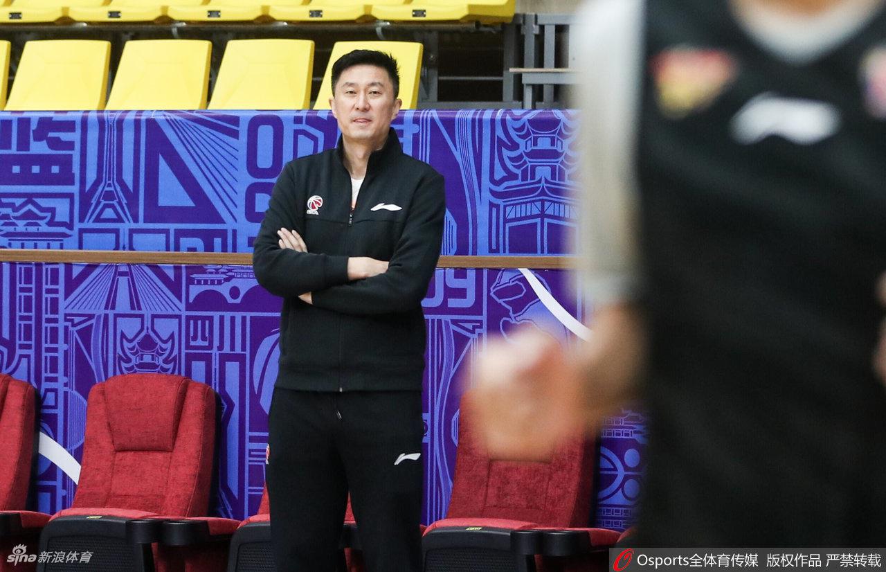 大汗淋漓的易建联在场边休息,用毛巾擦拭汗水,背景中可以看到空旷的看台和专注的队友