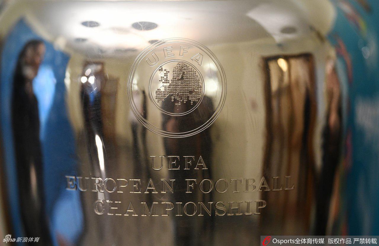 吉祥物斯基尔齐双手指向天空，仿佛在呼唤全欧洲的球迷关注它身旁那座闪耀着银色光芒的德劳内杯