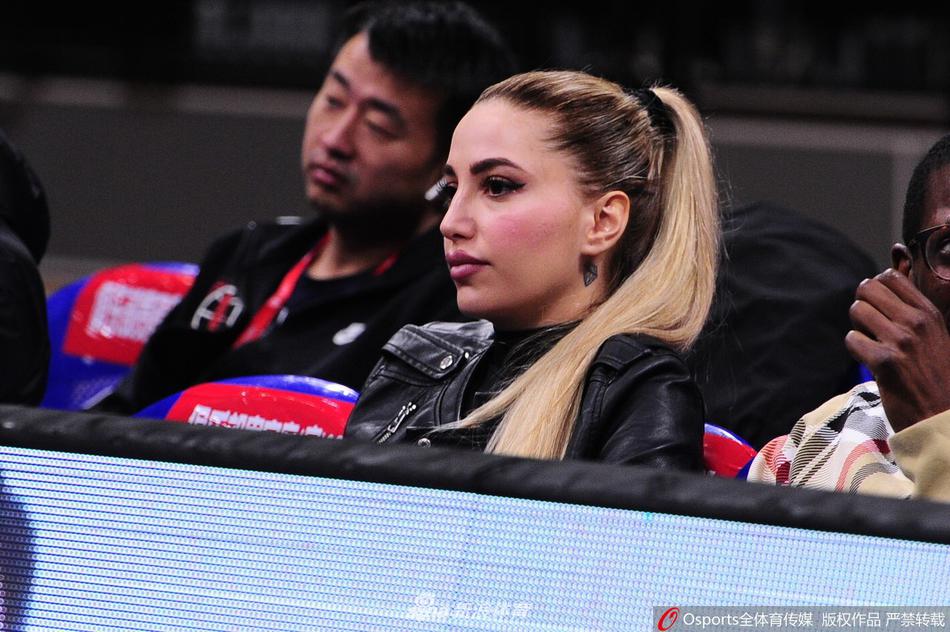 一位戴着可爱毛线帽的女球迷，双手捧着手机认真地进行自拍，身后是热血沸腾的赛场和正在激战的球员。她甜美的笑容与激烈的比赛形成了奇妙的和谐，记录下自己与辽篮共同度过的又一个难忘夜晚。