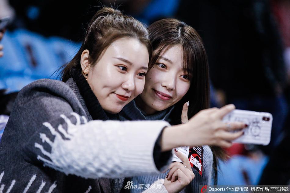 一位戴着黑框眼镜的北京首钢美女球迷，在吉林主场看台上绽放出明媚笑容，她身后是身穿绿色球衣的东北虎球迷，蓝绿交织间，凸显出客队球迷的勇敢与热爱。