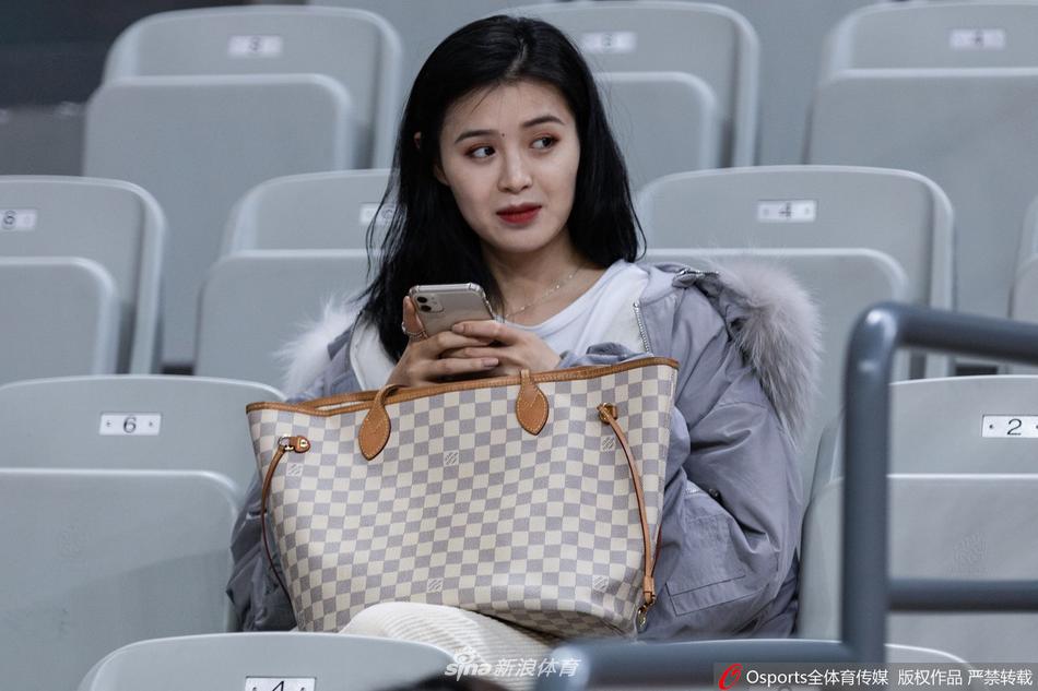 一位长发披肩的浙江金牛美女球迷，眼神专注地望着场内，精致的面容在球馆灯光下格外引人注目，她身着白色外套，成为看台上一道清新的风景。