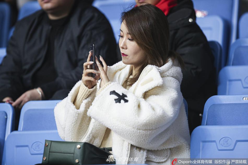 一位戴着眼镜的北京女球迷,面带温柔而满足的微笑,脸颊因为激动而微微泛红,在喧嚣的看台一角安静地注视着赛场,散发着温婉的知性美。