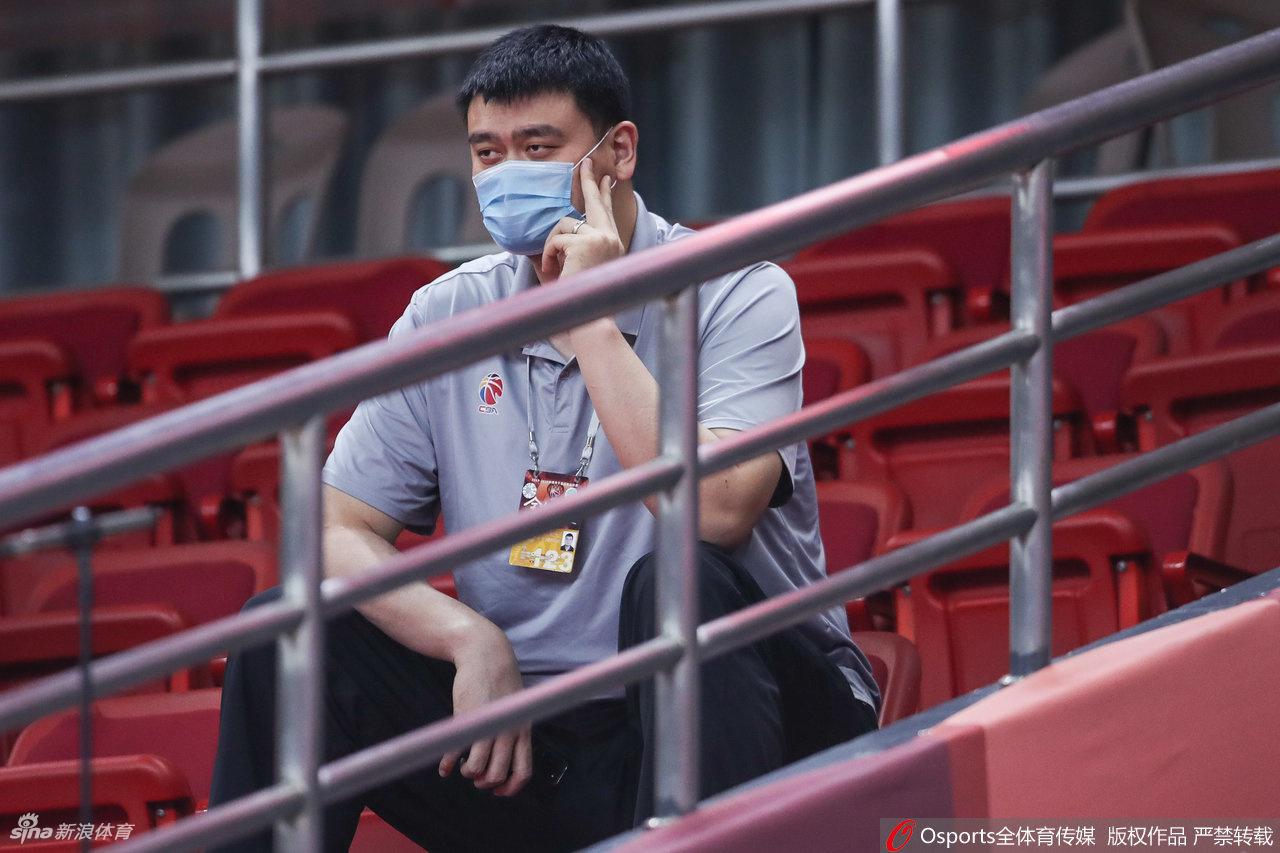 身形庞大的姚明独自端坐看台，深色口罩几乎遮住了大半张脸，只露出一双深邃而专注的眼睛，目光紧紧跟随着球场上的攻防转换。