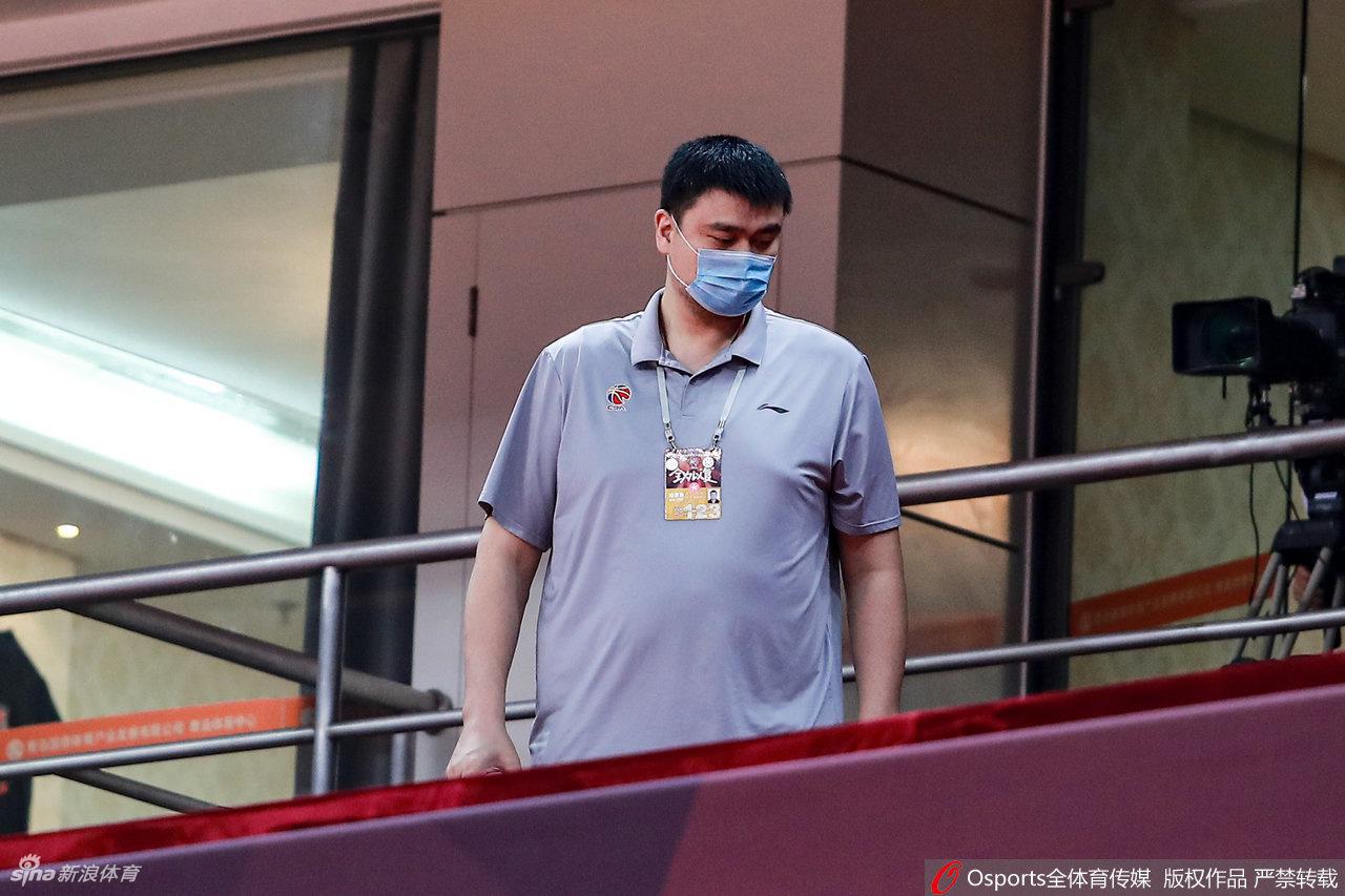 镜头拉近，姚明的眉眼间写满凝重，他下意识地微微低头，似乎正在思考球队的战术轮换或是联赛的长远规划，口罩的带子在他耳后勒出浅浅的印记。