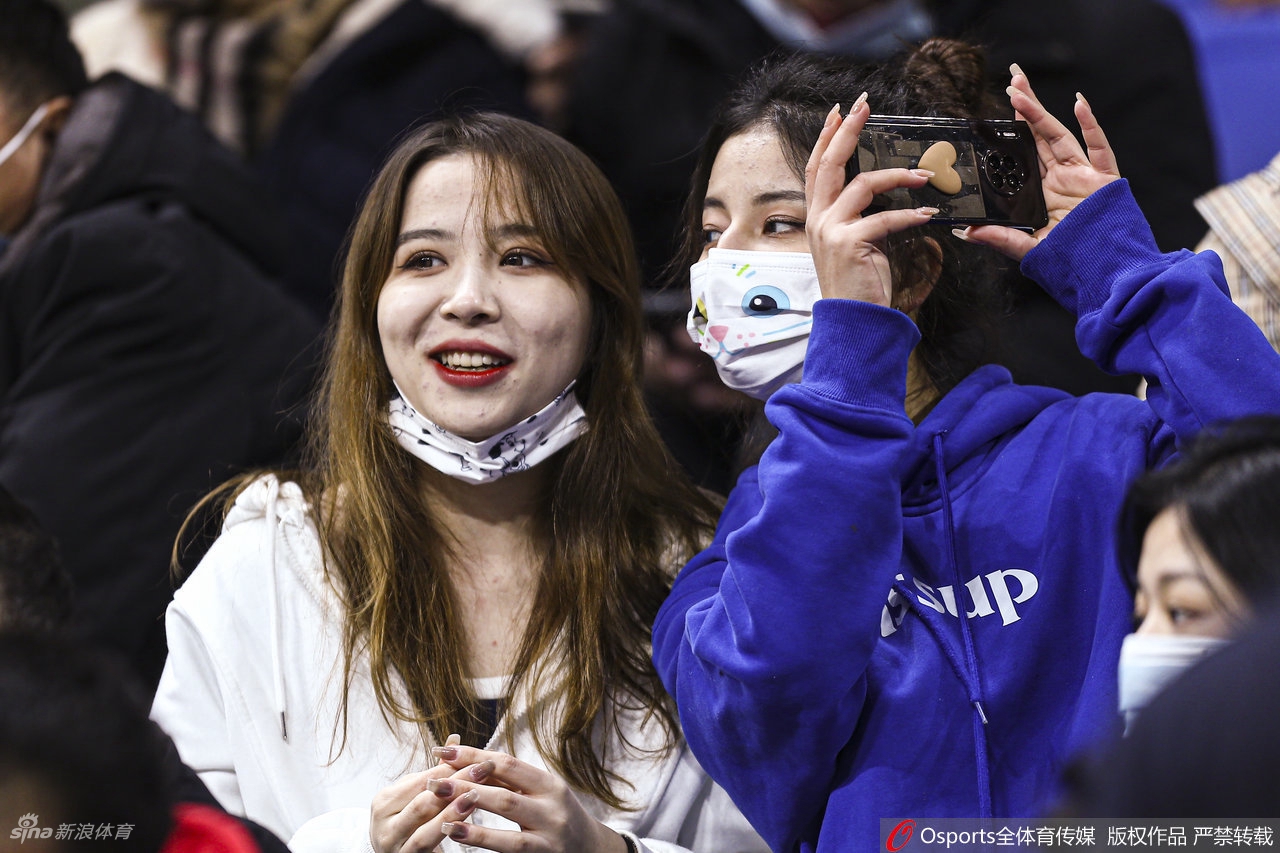 一名留着干练短发、穿着深色外套的女球迷正用手机记录赛场，她的神情认真而专注，仿佛要将这一刻的欢呼与呐喊都封存进小小的屏幕里，留待日后回味。