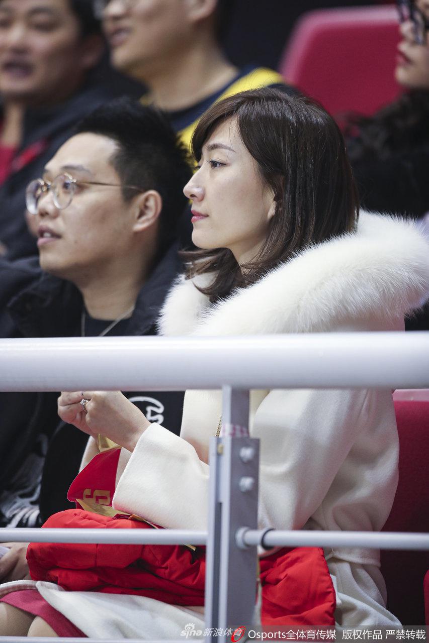 一位戴着眼镜的南京女球迷,双手轻轻合十抵住下巴,神情专注而虔诚,仿佛在用无声的祈祷为场上落后的主队加油鼓劲,背景里是模糊的赛场灯光。