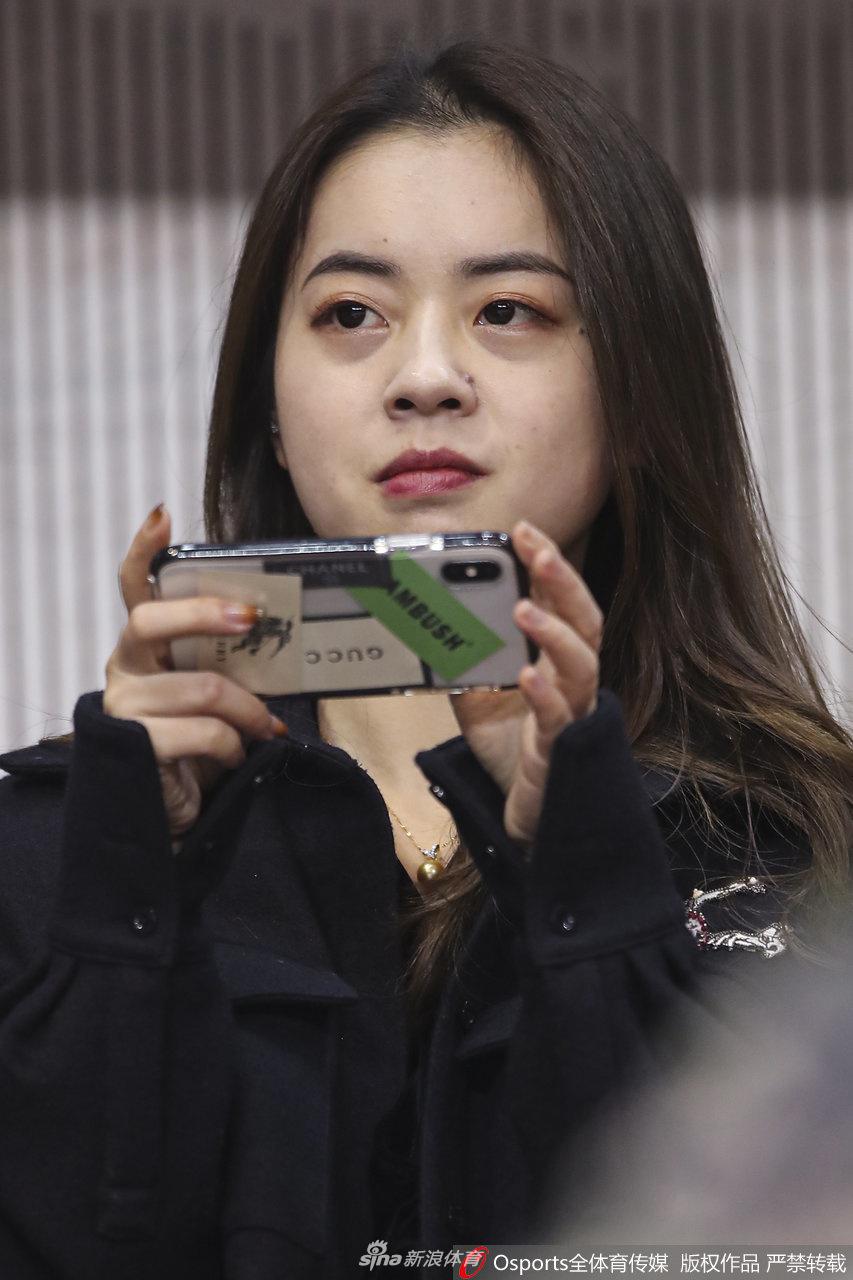 看台上一位长发披肩的年轻女球迷,利用比赛间隙低头查看手机,屏幕的亮光映照在她清秀的脸庞上,或许她正在和朋友实时分享此刻激动的心情。