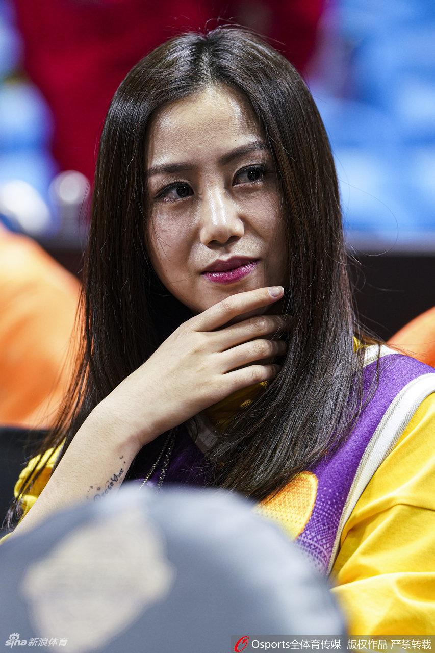 另一位观赛的女士气质优雅出众，她手持手机记录场上的精彩瞬间，侧颜线条优美，专注的神情显示出对比赛的高度投入。