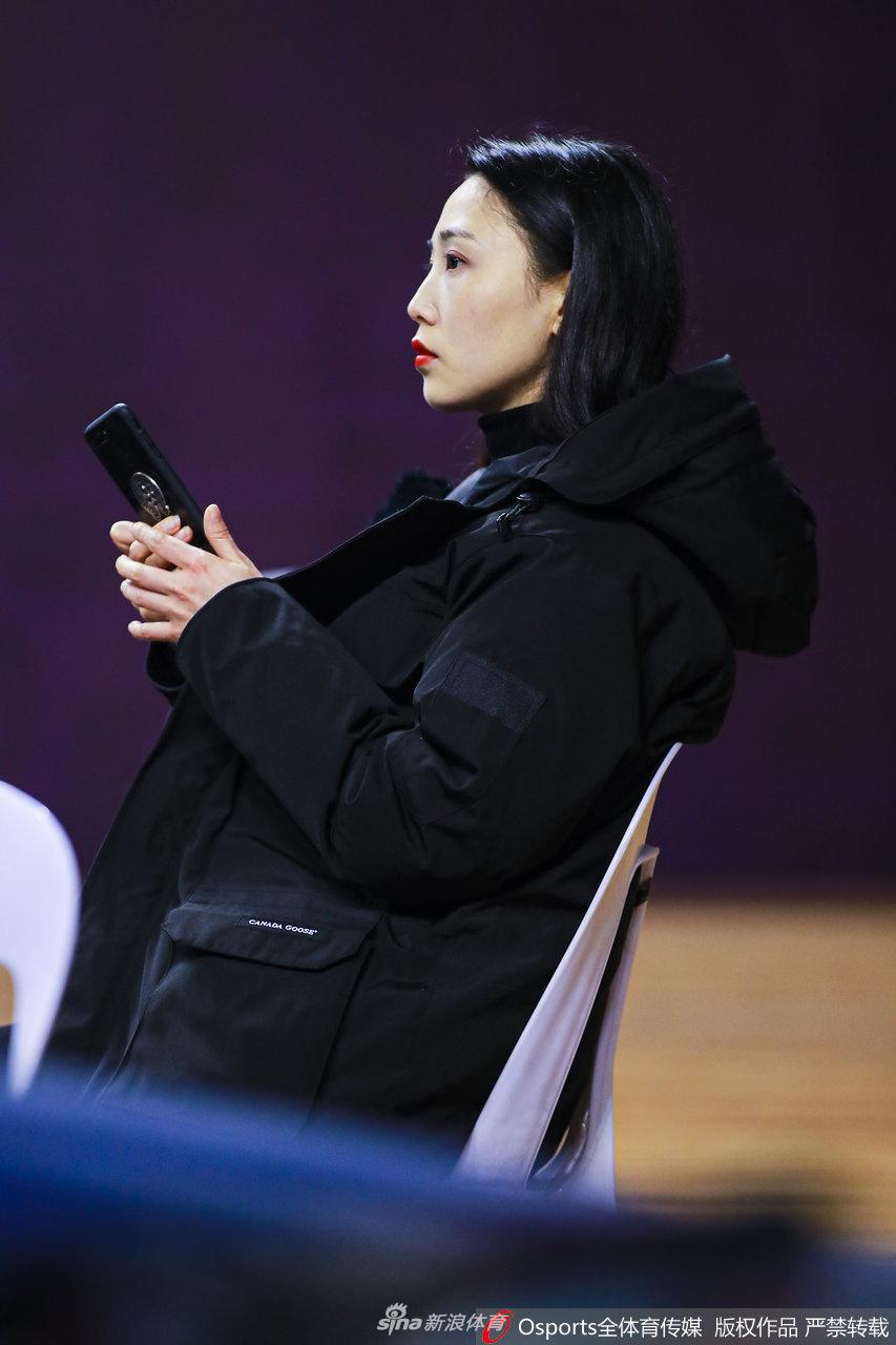 一位腼腆的小女孩紧紧抓着吉祥物的手指，回眸看向镜头，背景是忙碌的赛场工作人员，定格了喧嚣中最宁静的一刻。