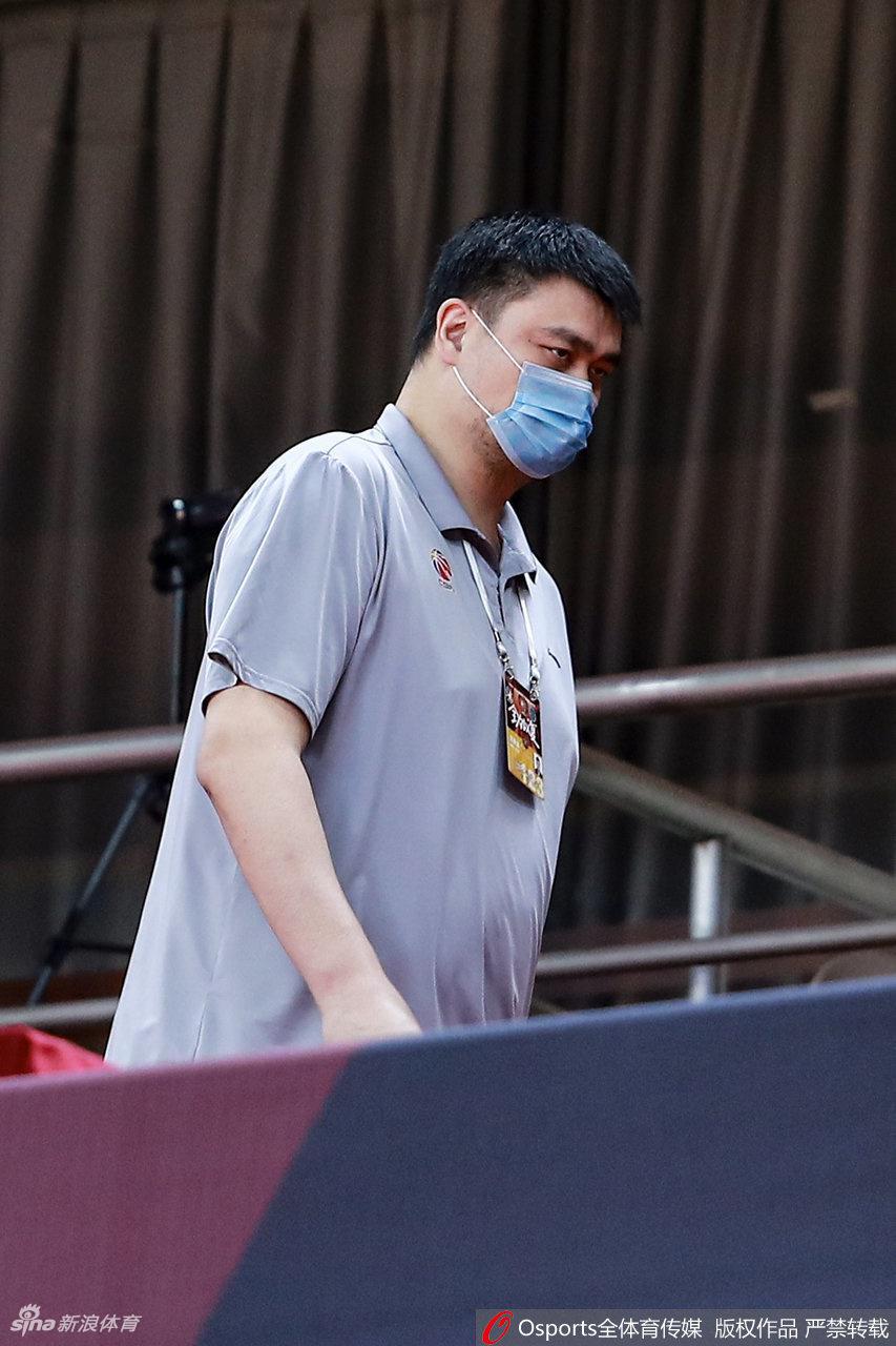 姚明侧身倚靠在座椅上，尽管口罩遮面，却遮不住他眉宇间的严肃与关切。空旷的看台放大了他的孤独，也凸显了他作为联赛守护者的责任与担当。