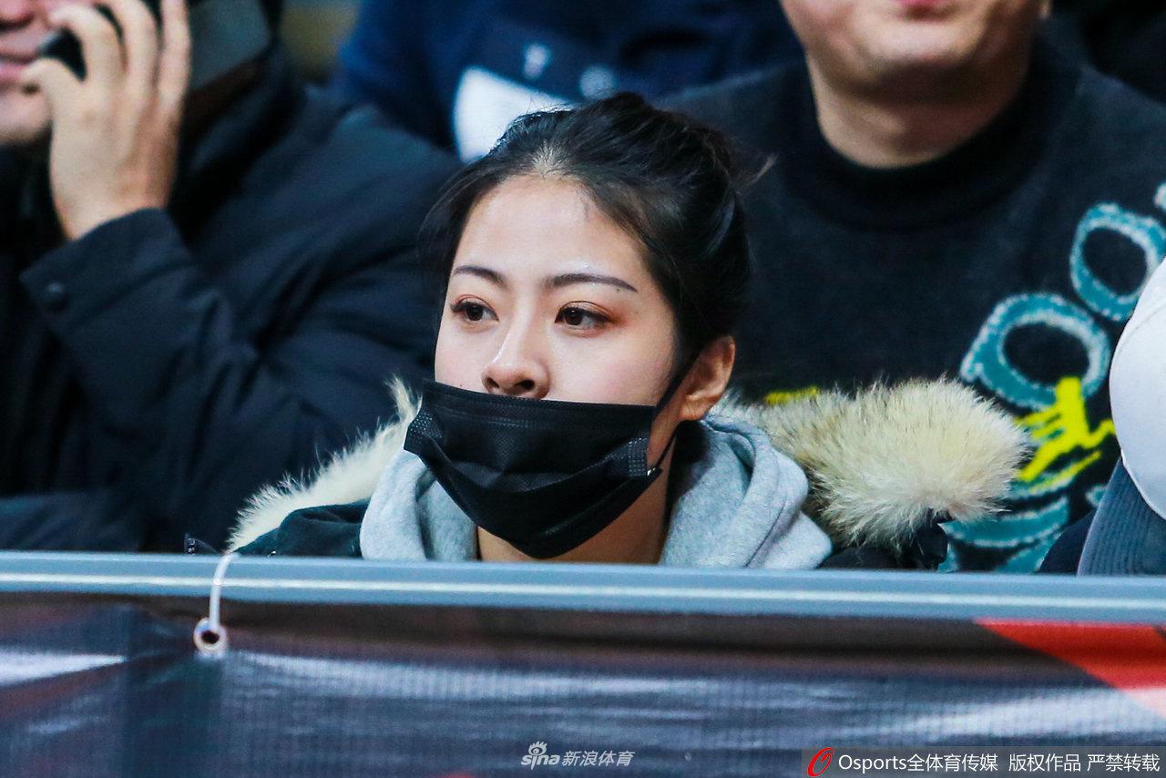 美女球迷低头查看手机,嘴角带着一丝微笑,可能在和朋友分享此刻赛场上的精彩瞬间。