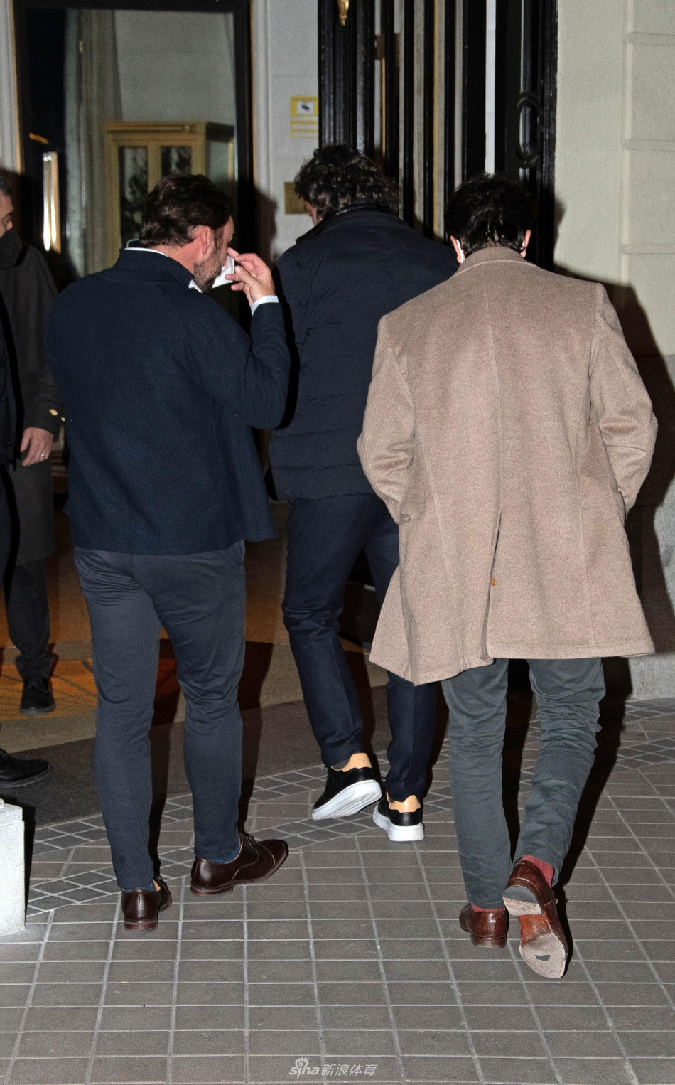 莫拉塔身穿深色大衣，在街道转角处与经纪人深入交流，眼神中透露出对未来的思考与决断。