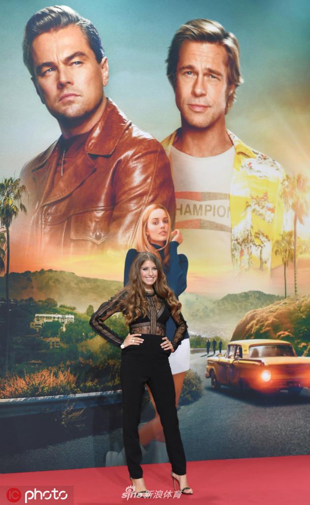 在签名区驻足，凯茜手持精致手包，侧身展示礼服的背部设计，流畅的线条与她的优雅姿态相得益彰，尽显时尚品味。