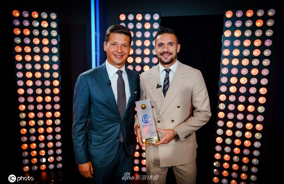 主教练滕哈格手捧象征着赛季最佳教练的橙色奖盘，目光坚定。身后的巨幅屏幕上正回放着球队夺冠的瞬间，这一刻的荣誉属于他和他的战术板，也属于每一位拼搏的弟子。