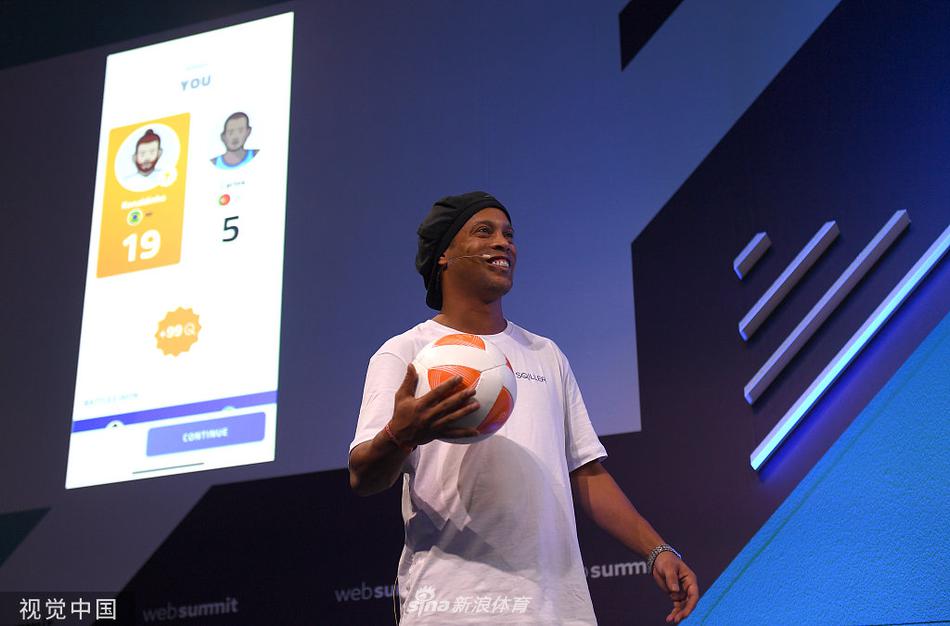 罗纳尔迪尼奥站在里斯本网络峰会的主背景板前，双手插兜，眼神自信，背景板上印有Web Summit 2019的巨大Logo