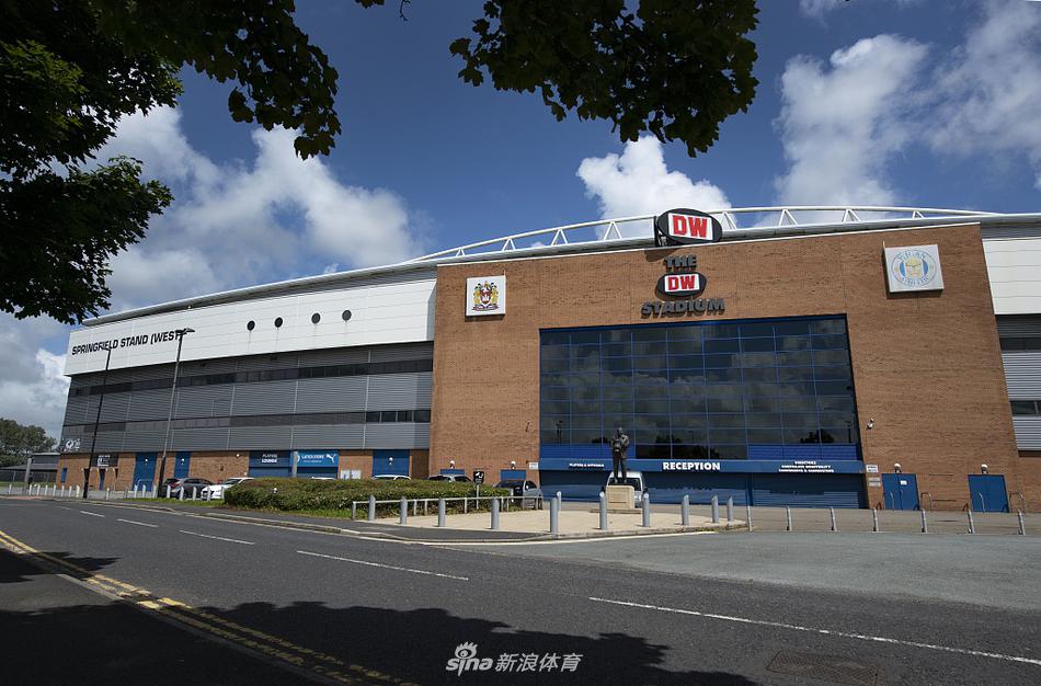 巨大的钢结构桁架如飞翼般从看台后方悬挑而出，其下是整齐的蓝红座椅，阳光透过桁架缝隙洒下斑驳光影，整个看台宛如一件静置于工业美学中的艺术品。