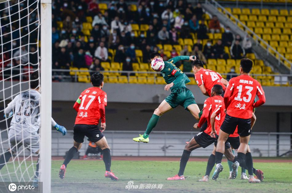 浙江绿城队长谈杨在成都双流体育中心高高跃起，以一记势大力沉的头槌攻破对方球门，背景是看台上密集的红色人海与瞬间凝固的兴城球迷