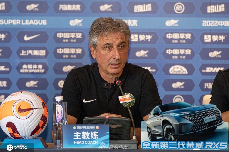 满头银发的主教练乔迪神情专注地对着话筒发言，身旁的球员董宇目光坚毅，两人身后的背景板上清晰印着中超联赛的标志，整个画面充满了大战前夕的凝重与期待。