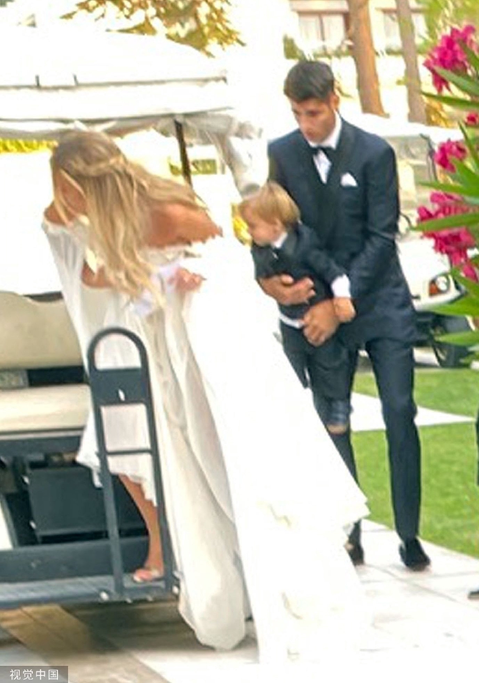 莫拉蒂单膝跪地，为妻子整理裙摆，眼神专注而充满爱意，妻子则含笑低头凝视，画面充满了自然流露的亲密与默契。