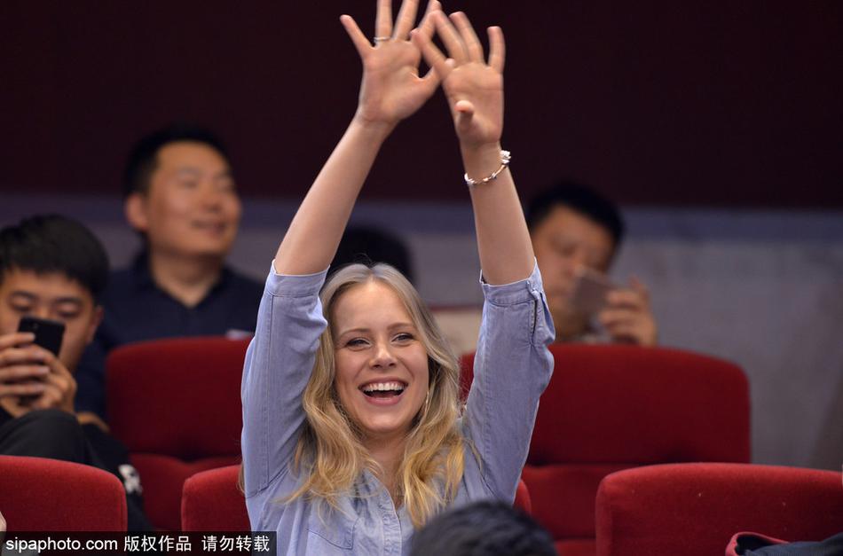 比赛间隙，宝莲娜探身望向球场方向，一头金色卷发在灯光下格外耀眼，眼神中流露出关切与期待，仿佛在用眼神与场上的丈夫交流。