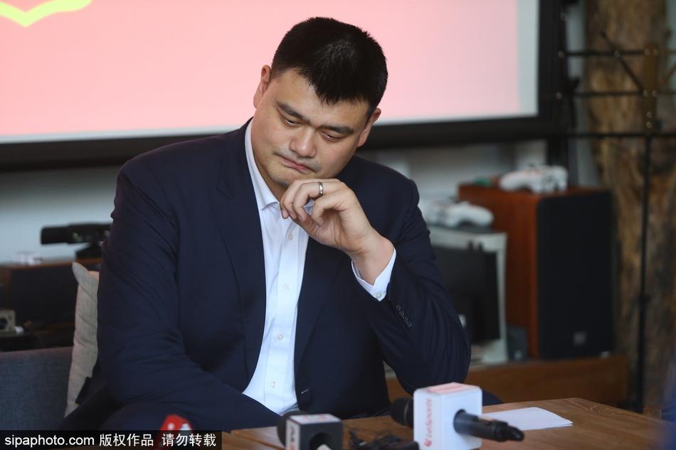 姚明在活动现场耐心倾听记者的提问，他的眼神专注而诚恳，周围摆放着简约的咖啡馆桌椅，透露出这次交流非正式的轻松基调。